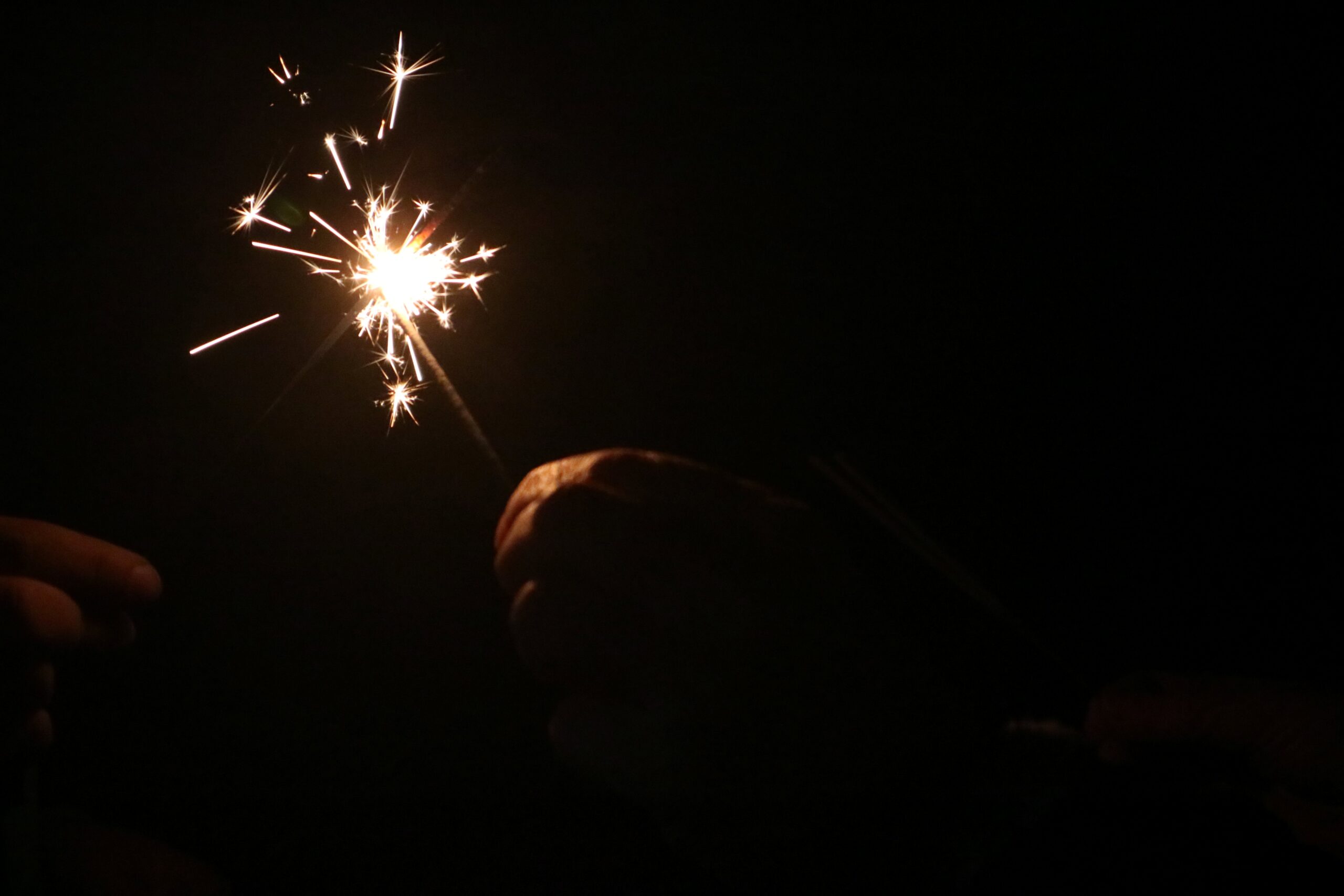 One hand holding a sparkler that another is reaching out to take.