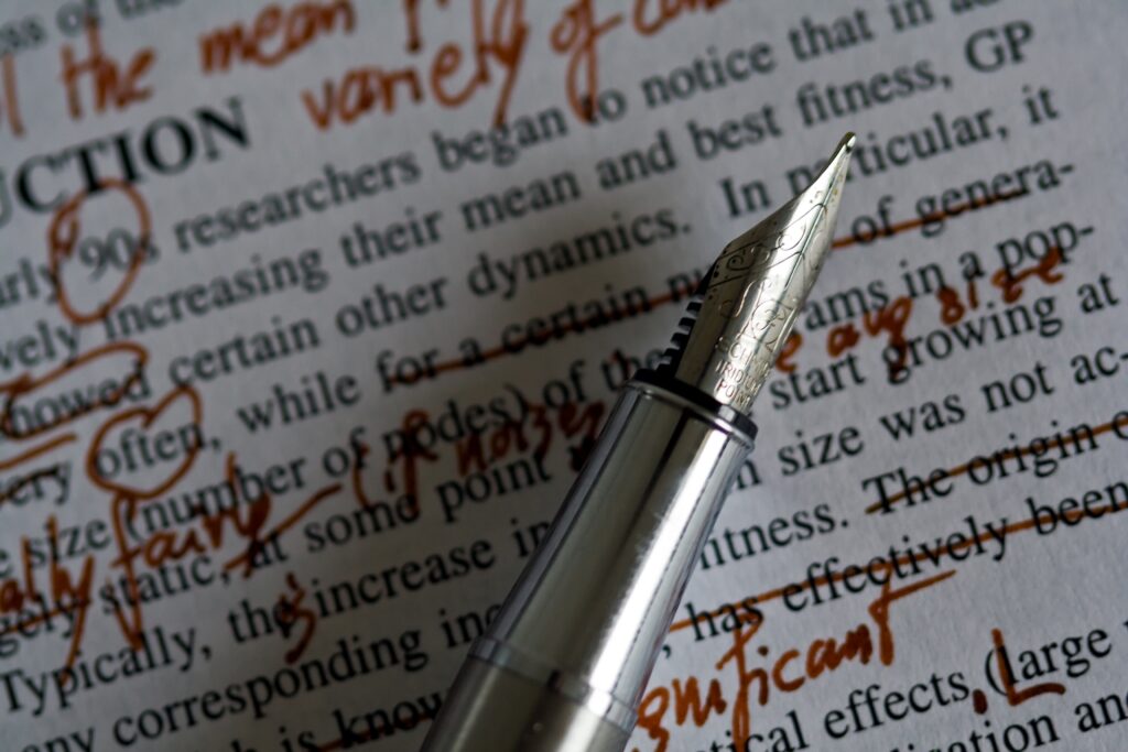 A fountain pen laid over a page with red annotations. Photo by Nic McPhee