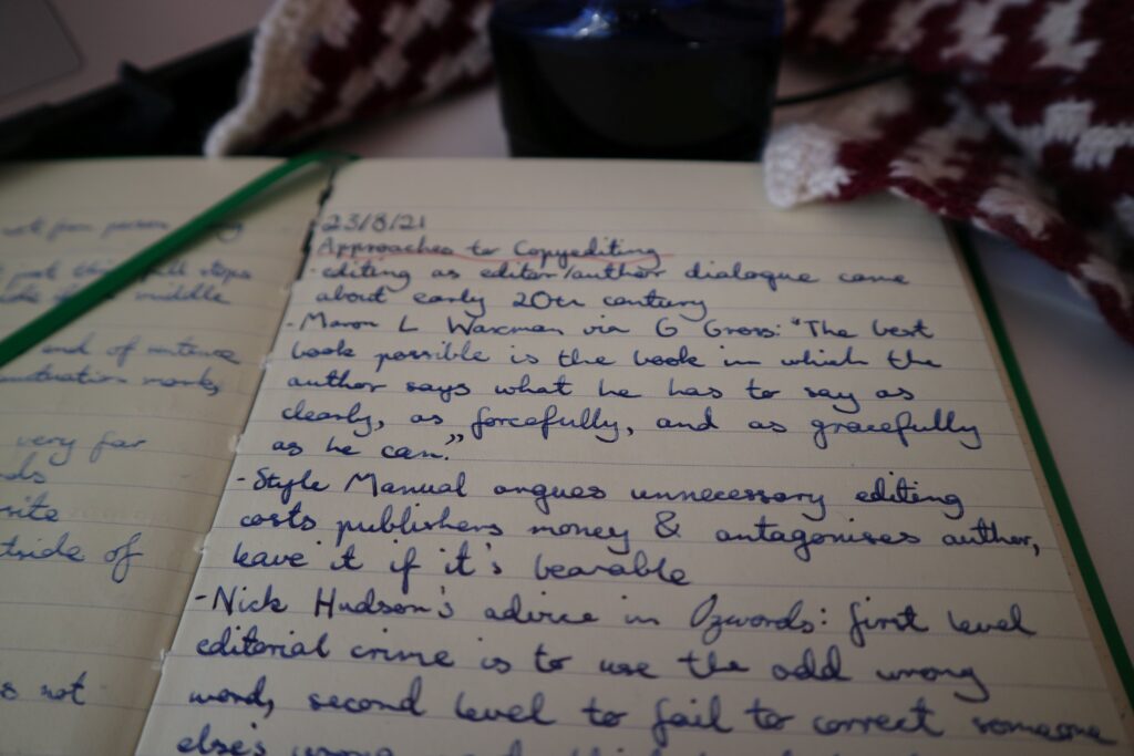 An open notebook, with a page of scribbled notes. In focus are the lines 'Mason [sic] L Waxman via G Gross: "The best book possible is the book in which the author says as clearly, as forcefully, and as gracefully as he can." and 'Style Manual argues unnecessary editing costs publishers money & antagonises author, leave it if it's bearable'