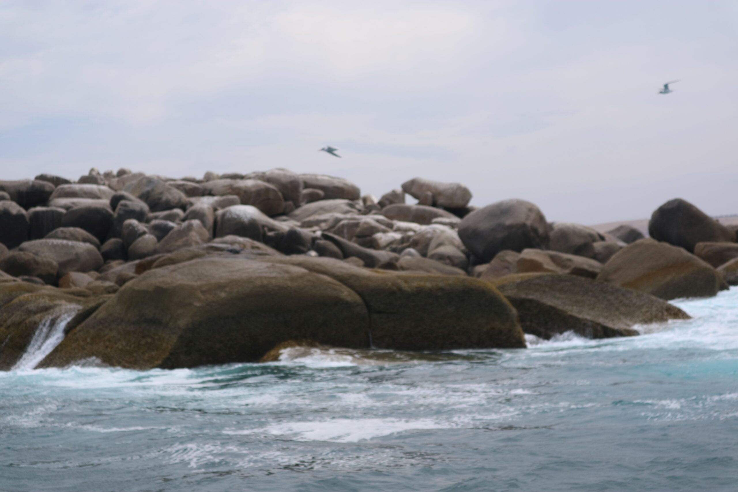 Waves slapping against grey rocks before a cloudy sky.